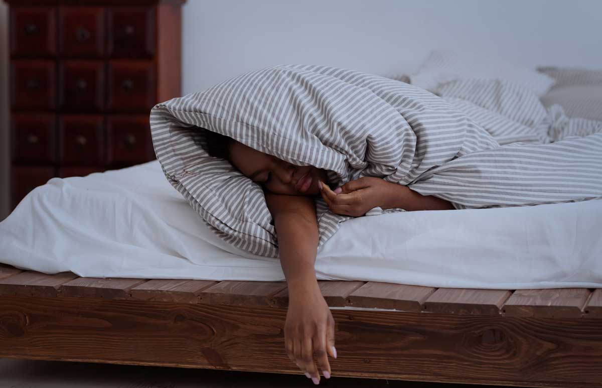 Ausreichend Schlaf, Tiefschlaf, Schlafstörungen, Probleme und Schlaflosigkeit in der Nacht. Traurige müde Frau in Decke schläft auf dem Bett im Inneren des Schlafzimmers, dunkel, Panorama, leerer Raum