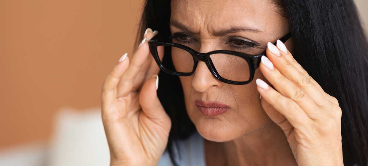 Reife Frau blinzelt, versucht durch Brille näher zu schauen