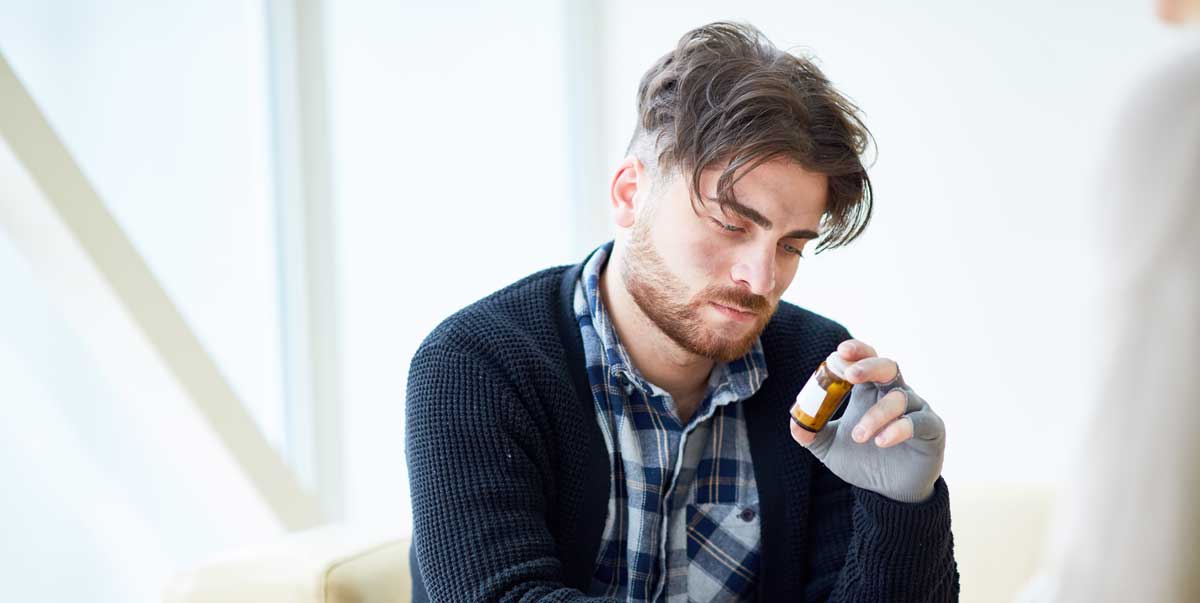 Bild, das eine Person in nachdenklicher Pose zeigt, die eine Pillendose in der Hand hält, um die Entscheidung zwischen Medikation und alternativen Behandlungsmethoden darzustellen.