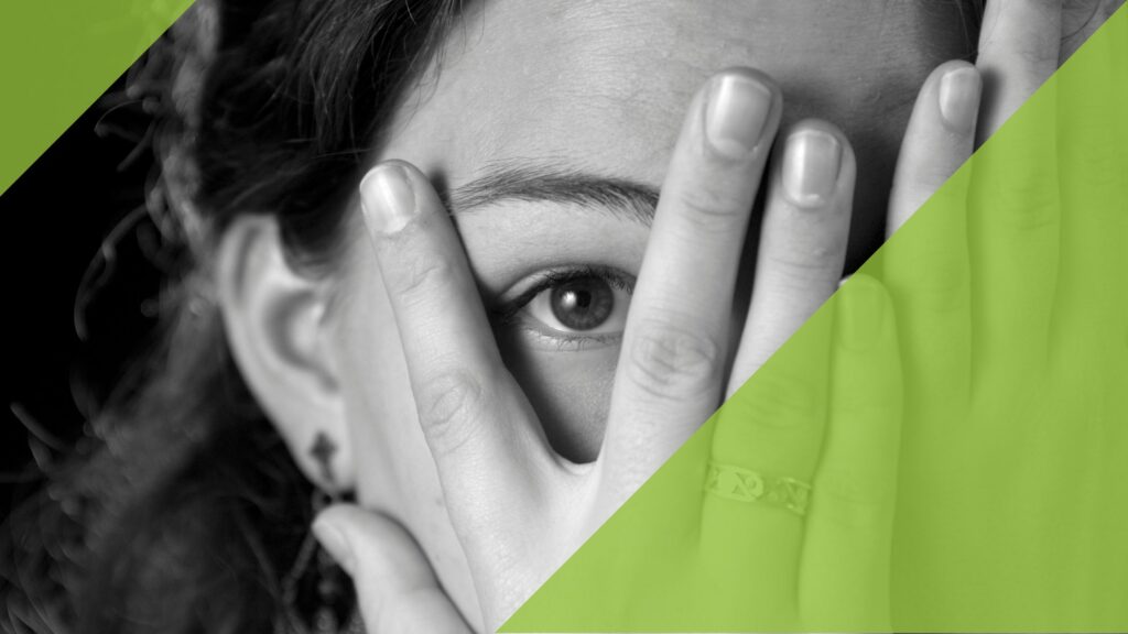 Frau, die durch gespreizten Finger der Hand schaut.