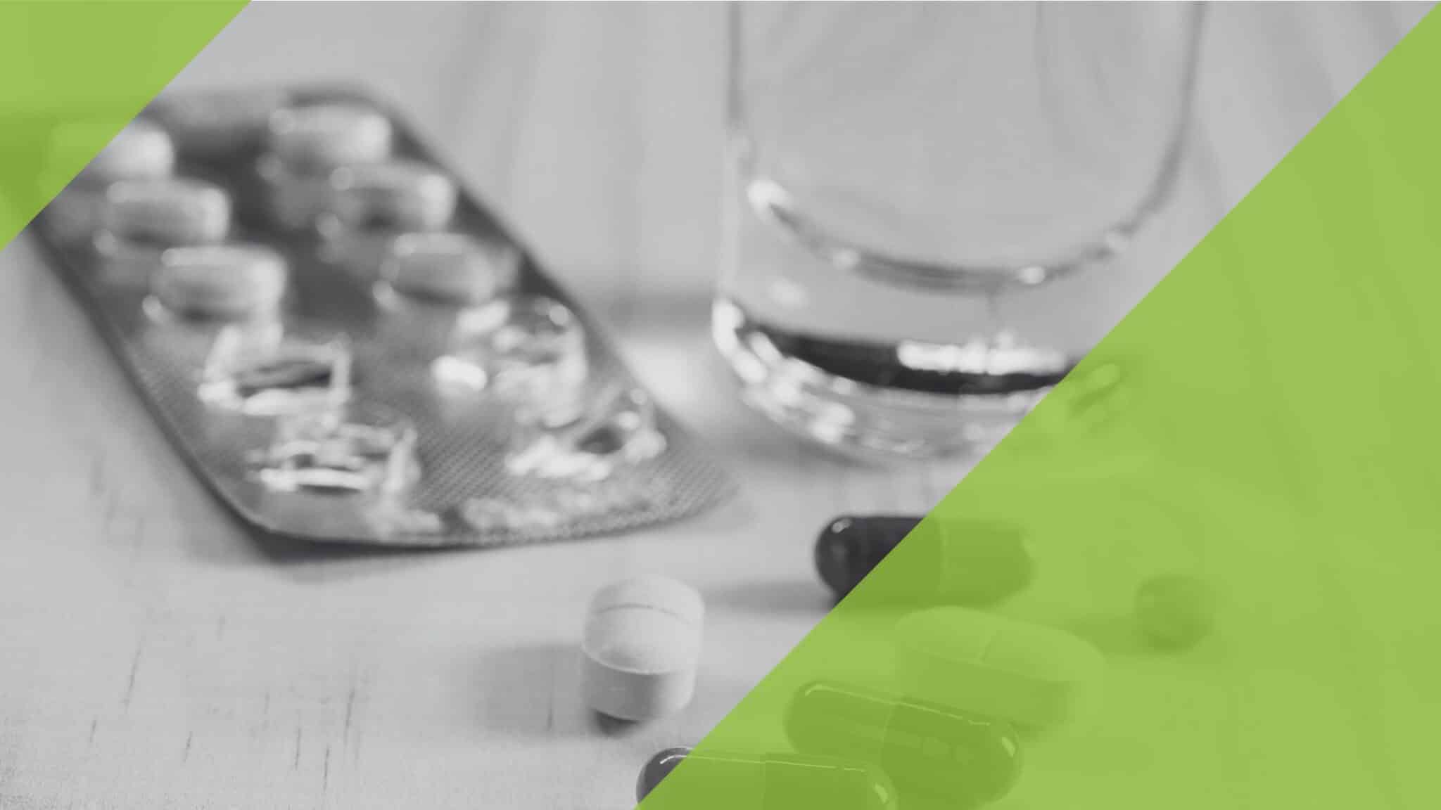 Verschiedene Tabletten und Kapseln liegen auf einem Tisch neben einem Glas Wasser.